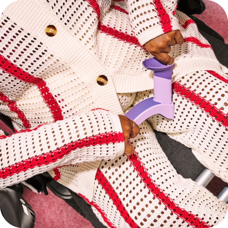 A person in a wheelchair wearing a white, knitted set with red vertical stripes. They are holding the tampon insertion aid.