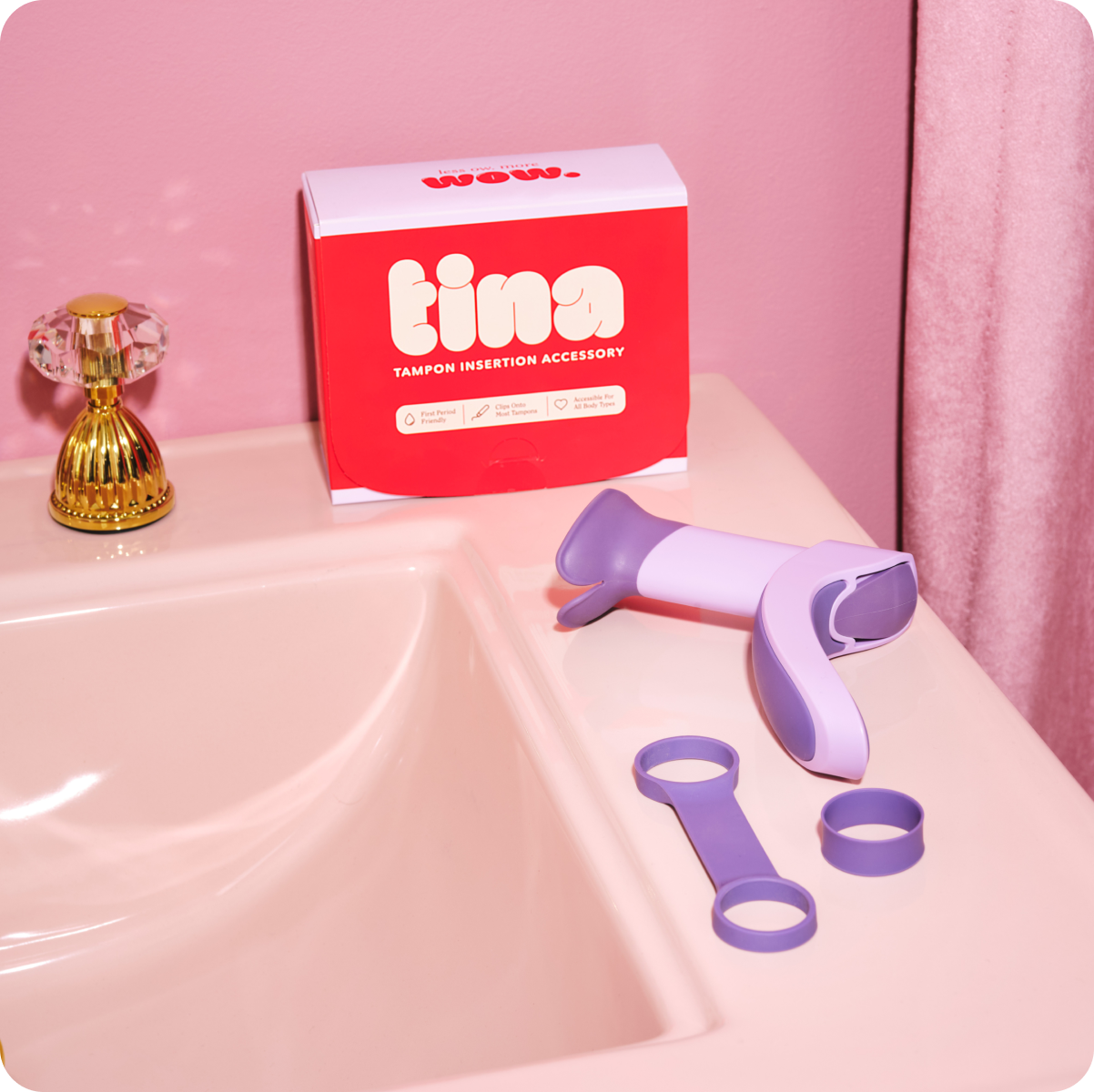 The tampon insertion aid sits on the side of a pink sink in front of a TINA-branded box.